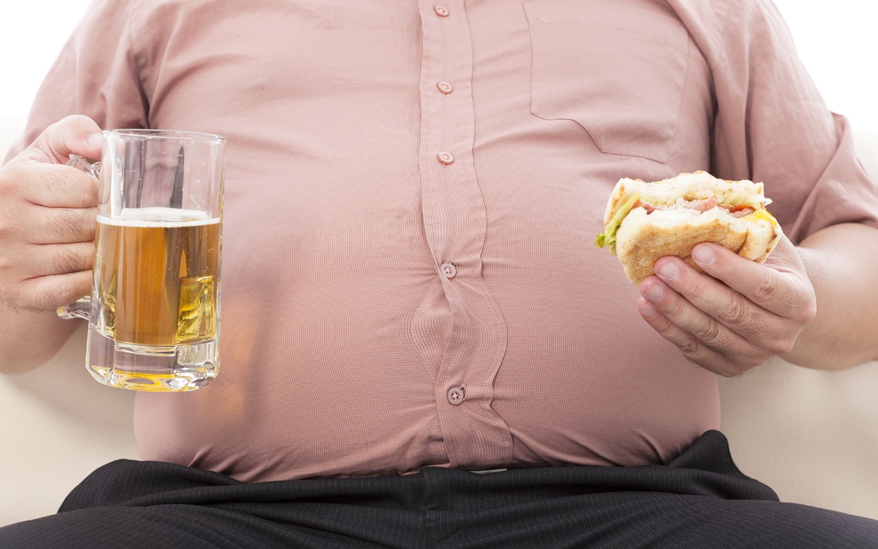 Ein dicker Mann mit einem Bier und einem Burger in der Hand