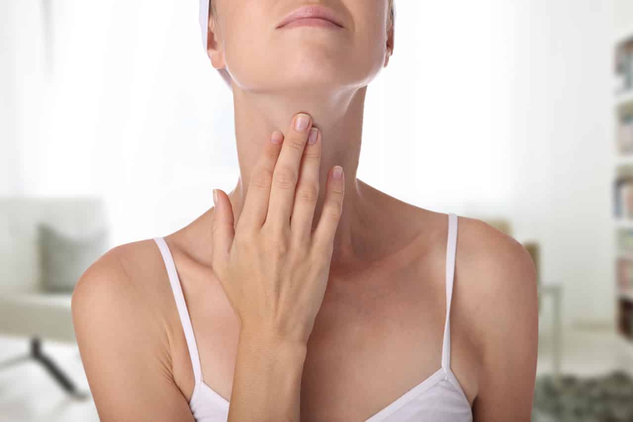 Eine Frau mit Stimmproblemen greift sich auf den Kehlkopf